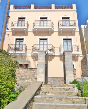 A multi-story building with balconies, stone steps leading to the entrance, and a clear sky. - Electra (Syros)