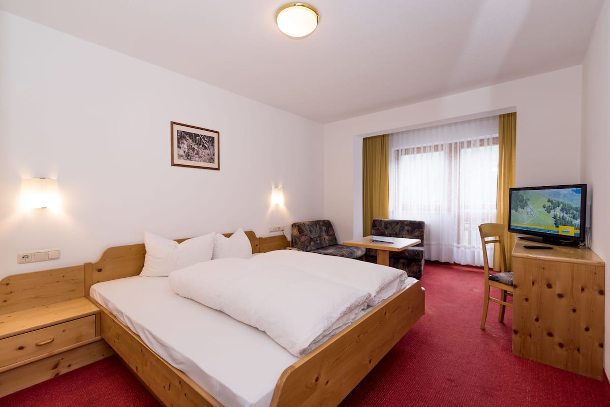 Una habitación de hotel con una cama de madera, un escritorio, una silla, un televisor y una ventana con cortinas.