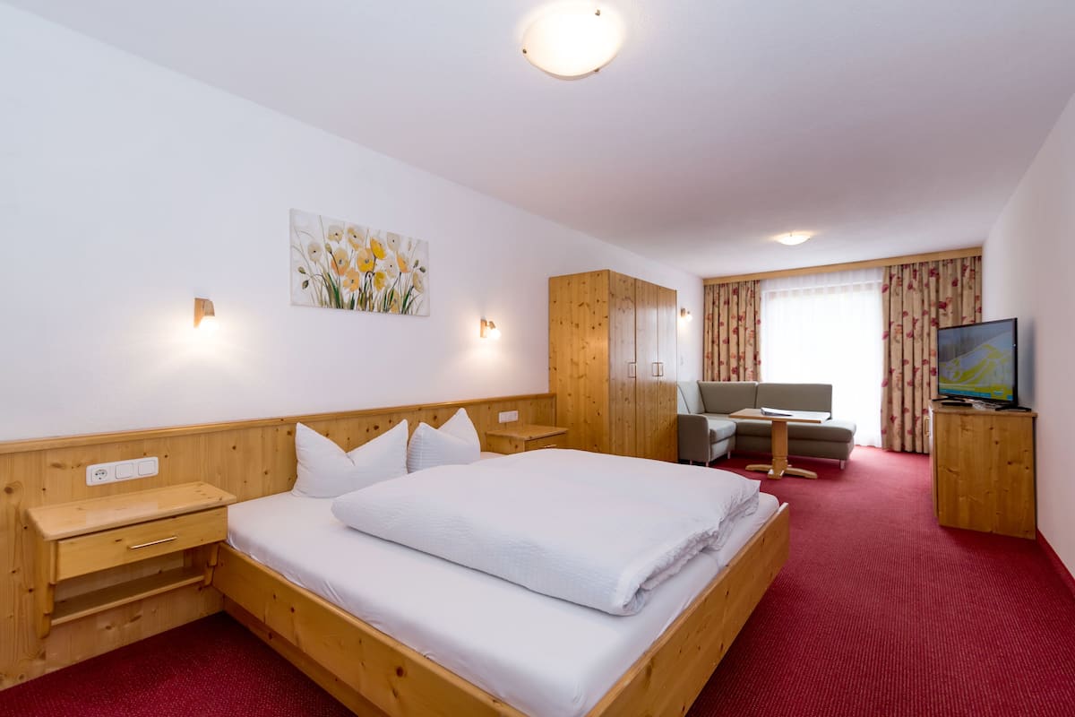 Una habitación de hotel con una cama de madera, un escritorio, un sofá y un televisor.