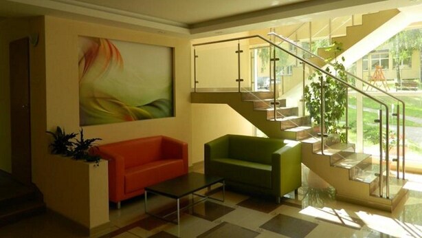 Un interior moderno con una escalera, un sofá rojo y verde, y un cuadro abstracto grande.