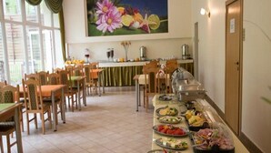 Un comedor con varias mesas y sillas, un bufé con diferentes opciones de comida y un cuadro de flores en la pared.