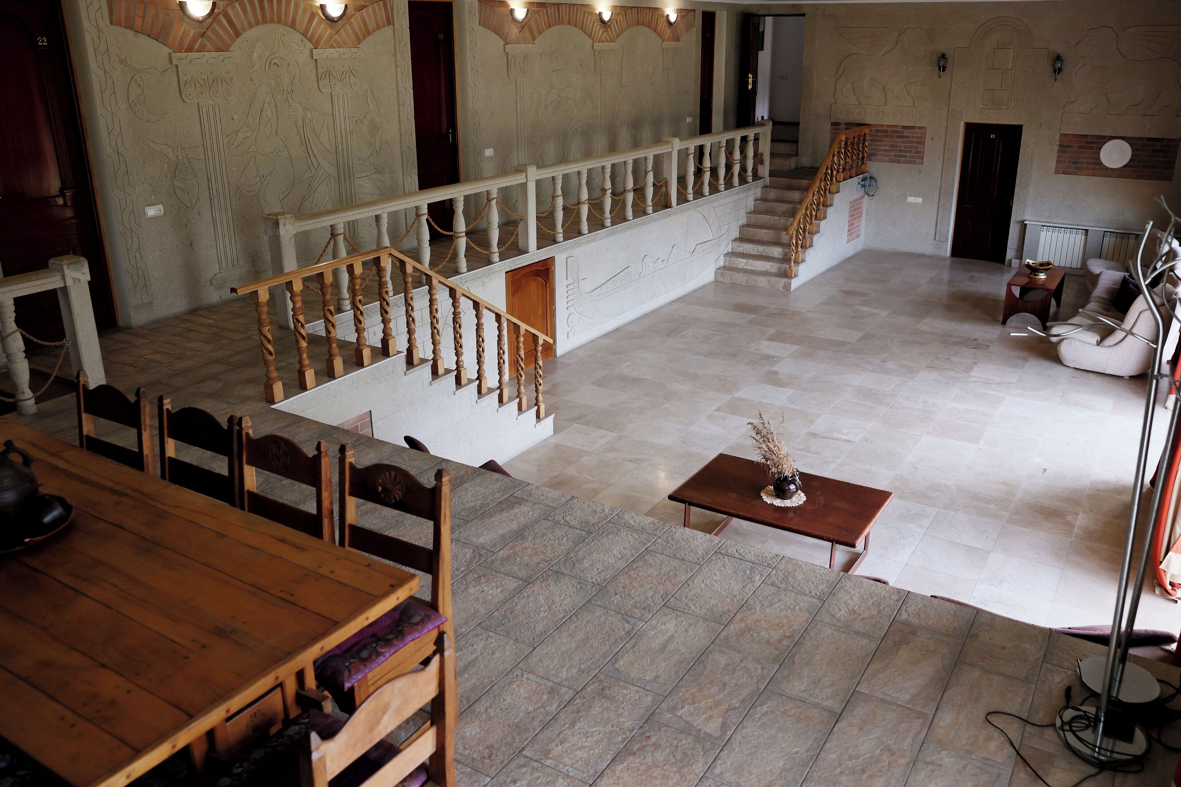 Um hall amplo com escada de madeira, área de estar com mesa e parede decorativa.