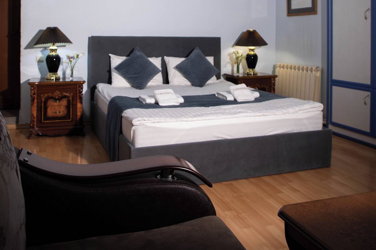 A neatly arranged bedroom with a bed, two bedside tables, a nightstand, a radiator, and a door.