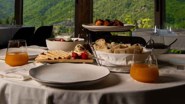Una mesa lista para el desayuno con vistas a la montaña, con platos, vasos y un bol de fruta.