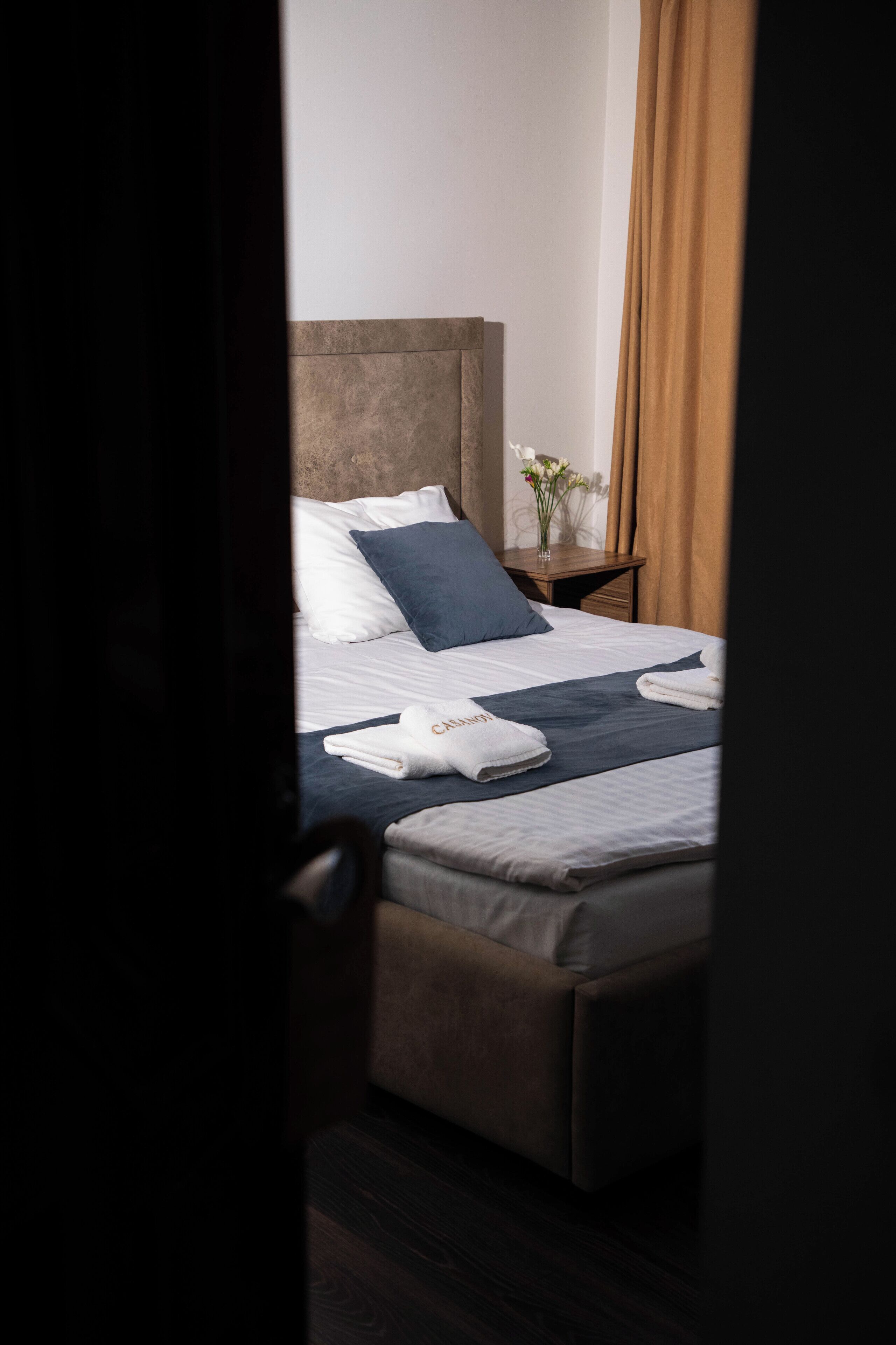 Una cama bien hecha con ropa de cama blanca y azul, un cabecero de madera y una mesita de noche con un florero.