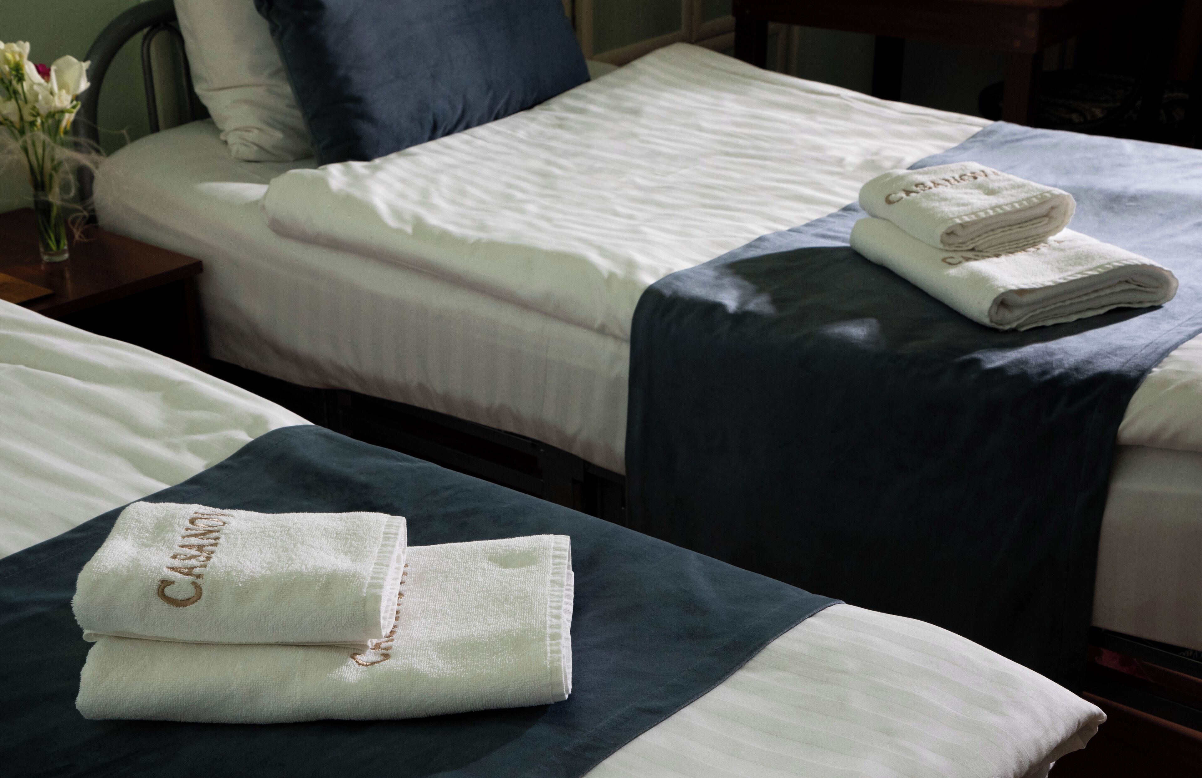 Una camera d'albergo con due letti, ognuno con copripiumino blu scuro e lenzuola bianche. Sui letti sono posati due asciugamani piegati con il nome dell'hotel.