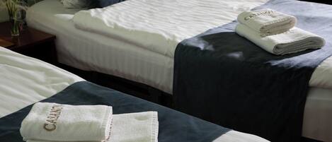 Una camera d'albergo con due letti, ognuno con copripiumino blu scuro e lenzuola bianche. Sui letti sono posati due asciugamani piegati con il nome dell'hotel.