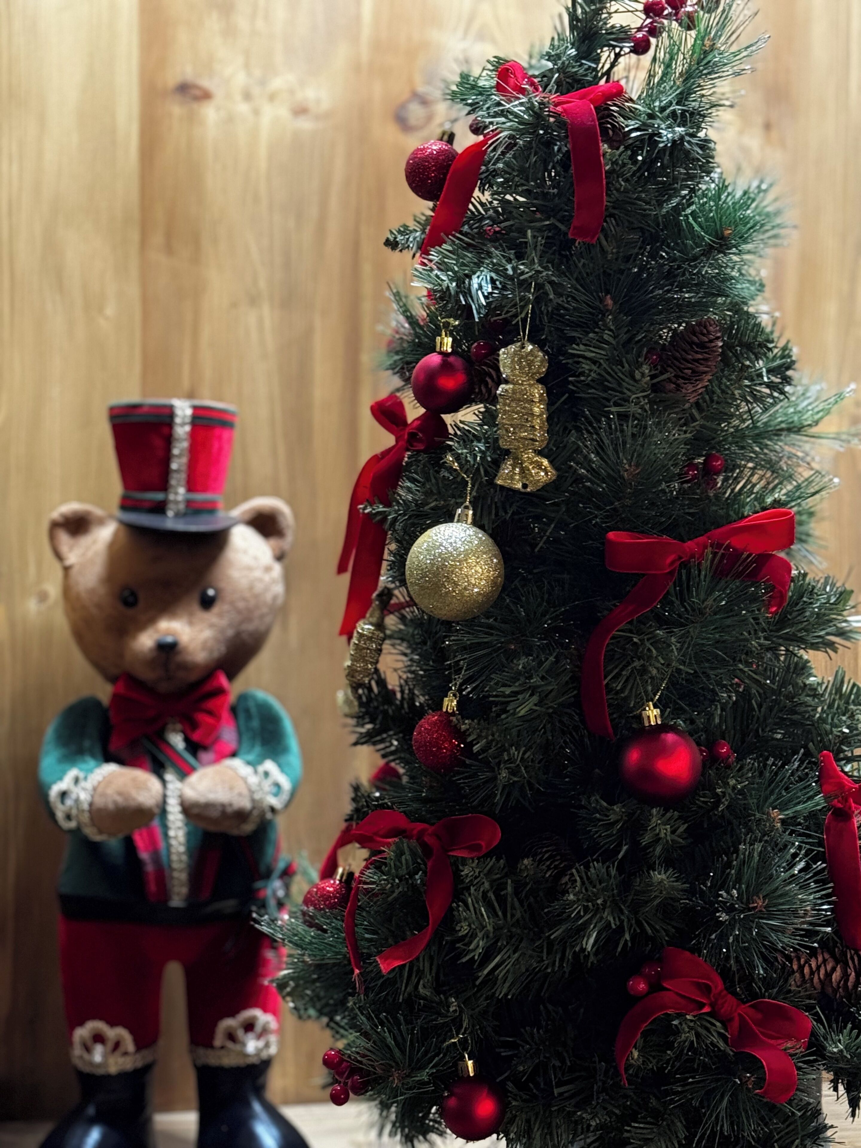 A Christmas tree with red and gold ornaments, ribbons, and a teddy bear figure.