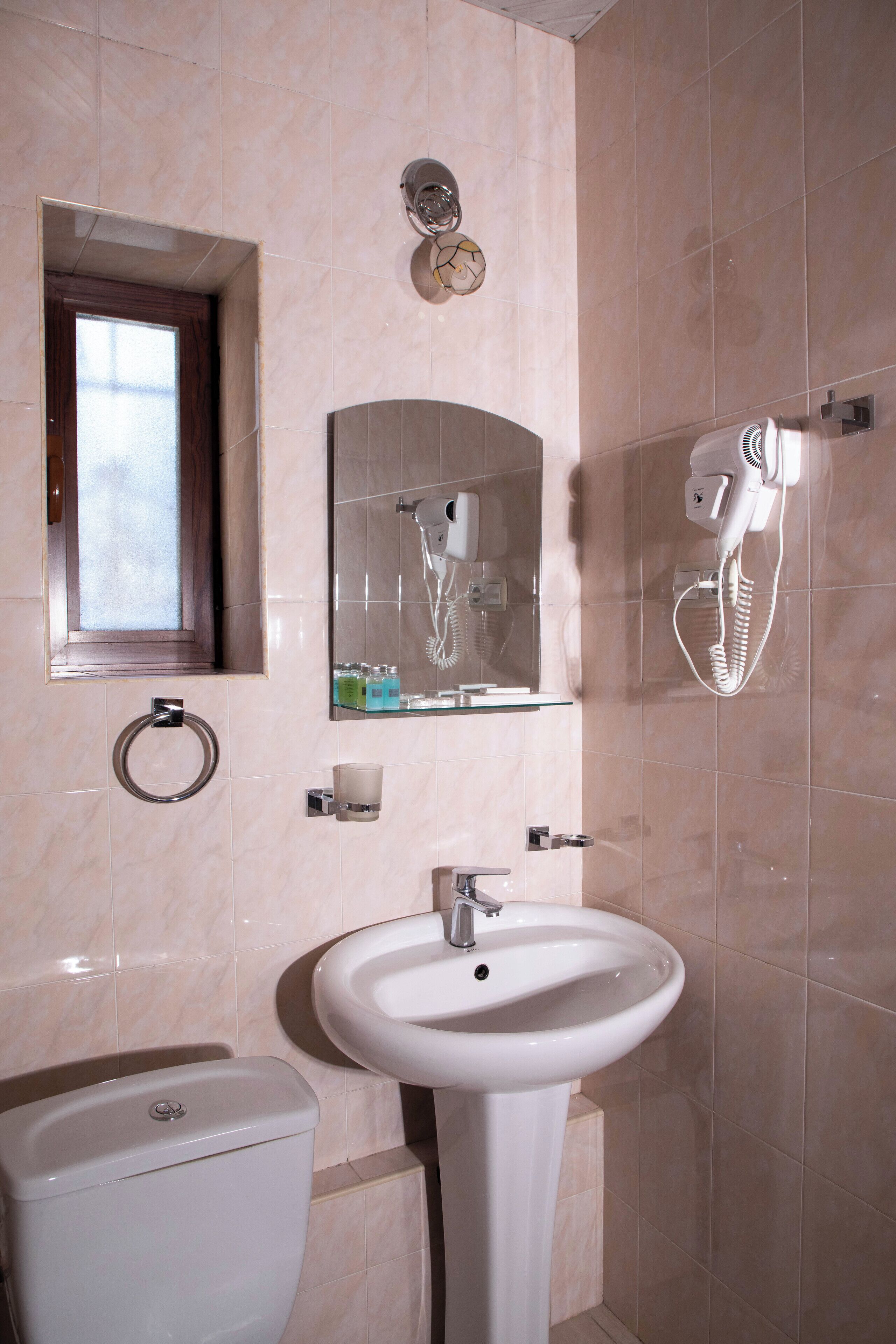 Un baño con inodoro, lavamanos y espejo con secador incorporado.