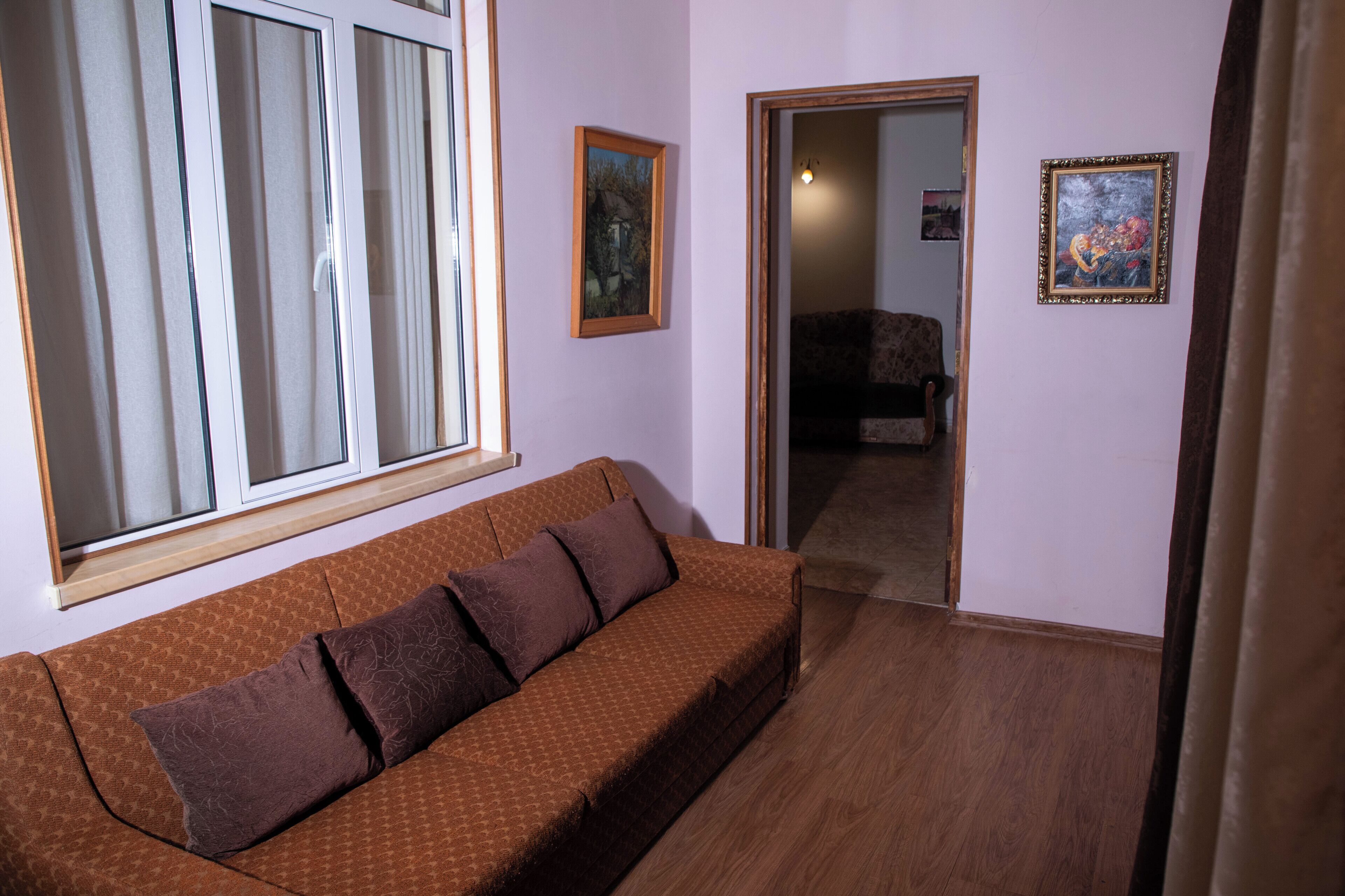 Ein Zimmer mit einem braun gemusterten Sofa, einem Fenster mit Vorhängen und zwei gerahmten Kunstwerken an der Wand.