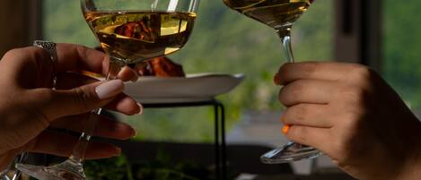 Two hands holding wine glasses with a scenic mountain view in the background.