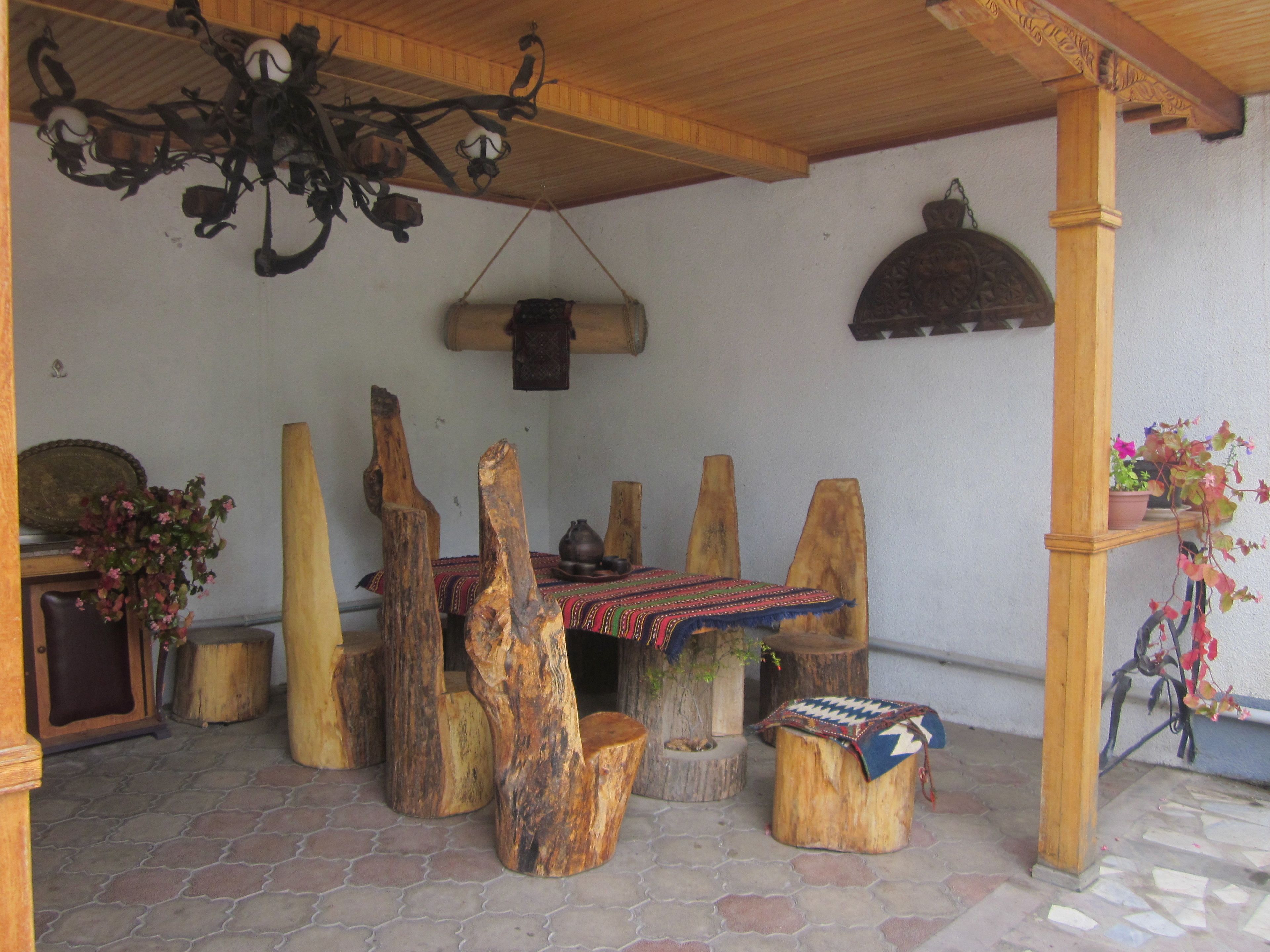 Zona de dinar rústica de fusta amb una taula i bancs fets de troncs d'arbre, una làmpada penjant i una planta en test a la dreta.