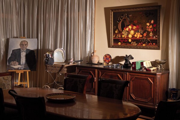 Un comedor con una mesa de madera, sillas, un cuadro y una naturaleza muerta de frutas en la pared.