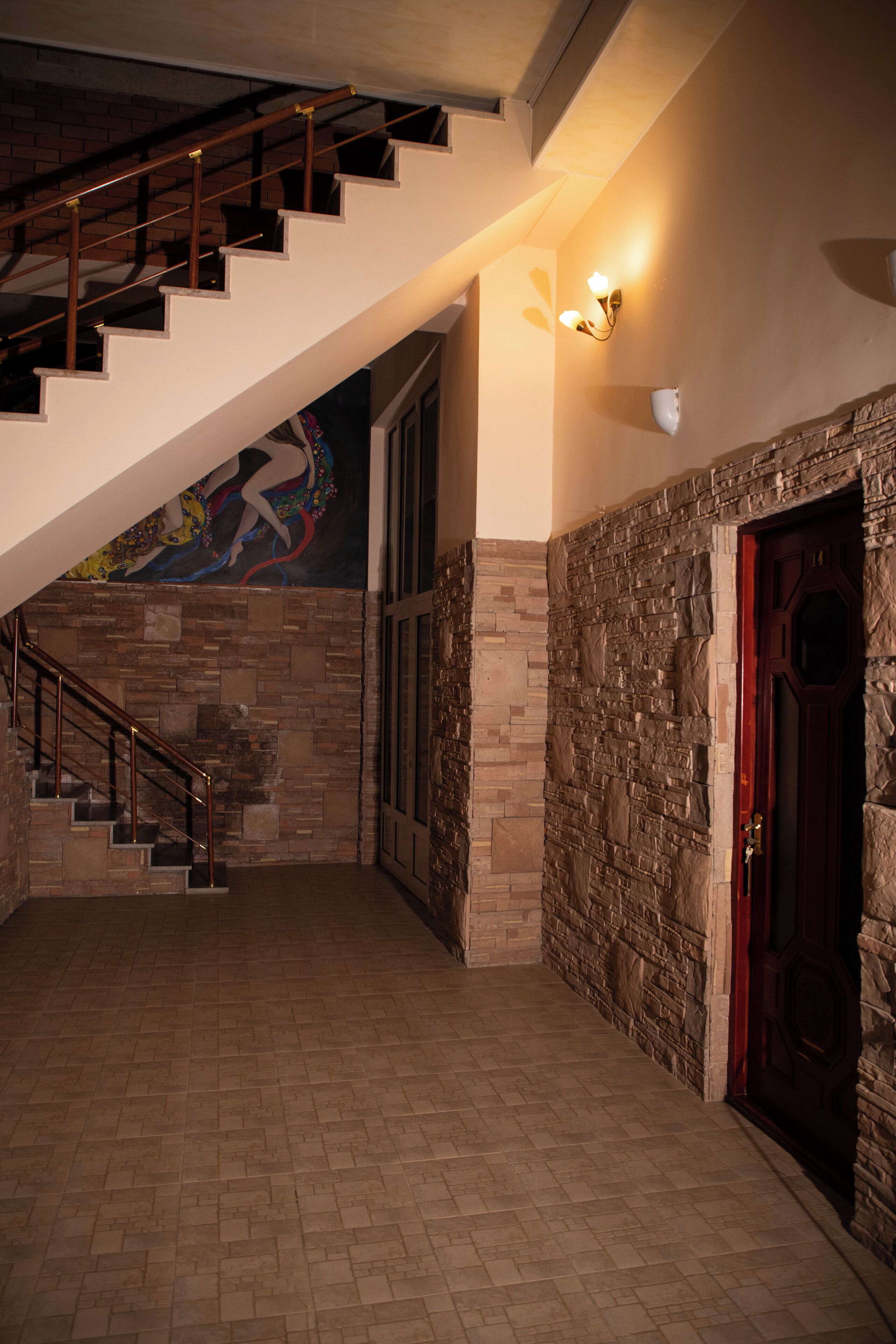 A staircase with a wooden handrail leading to a landing with a stone wall and a red door.