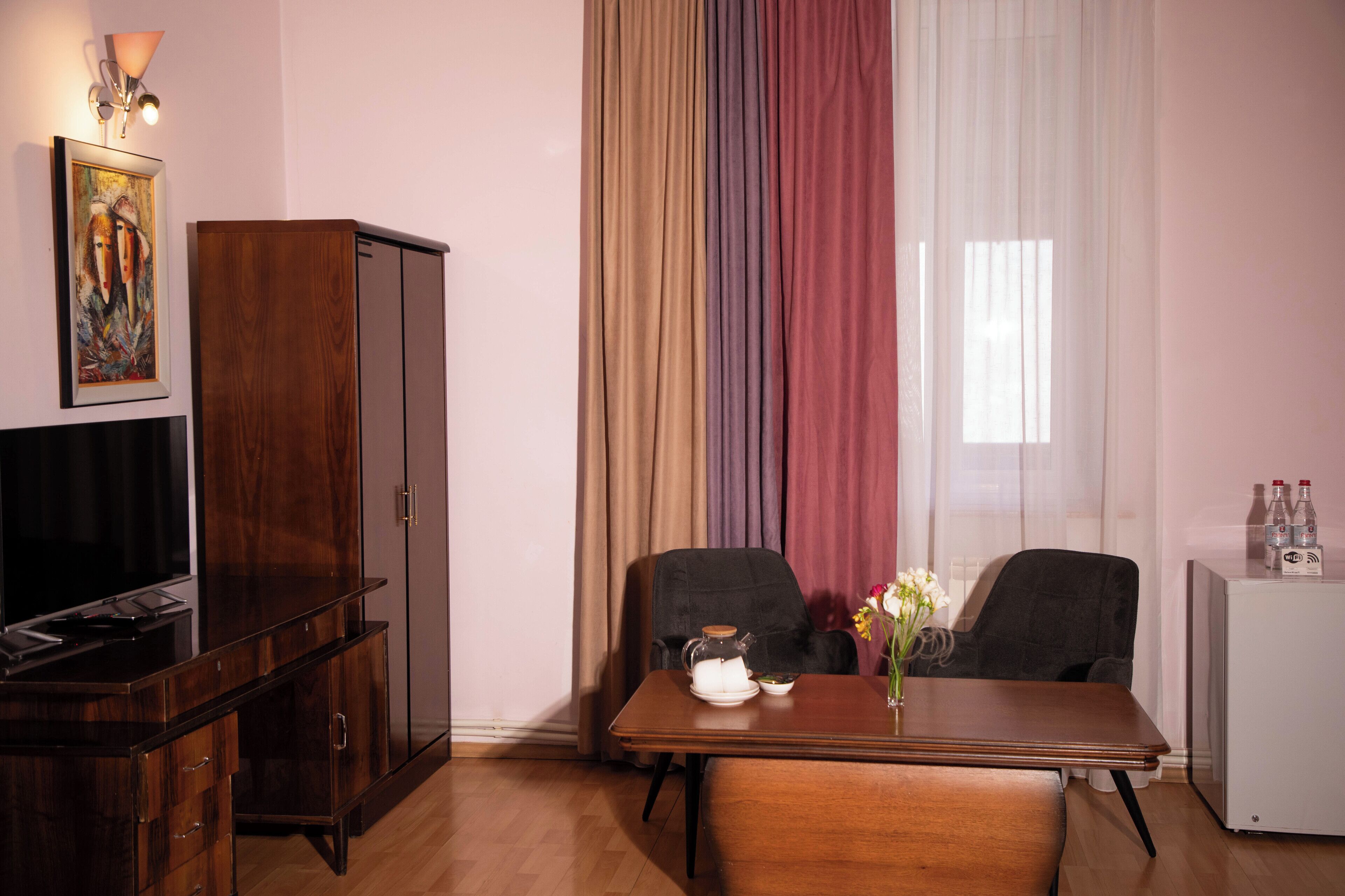 Une pièce comprenant un bureau en bois, deux chaises, un téléviseur, un meuble et une fenêtre avec des rideaux.