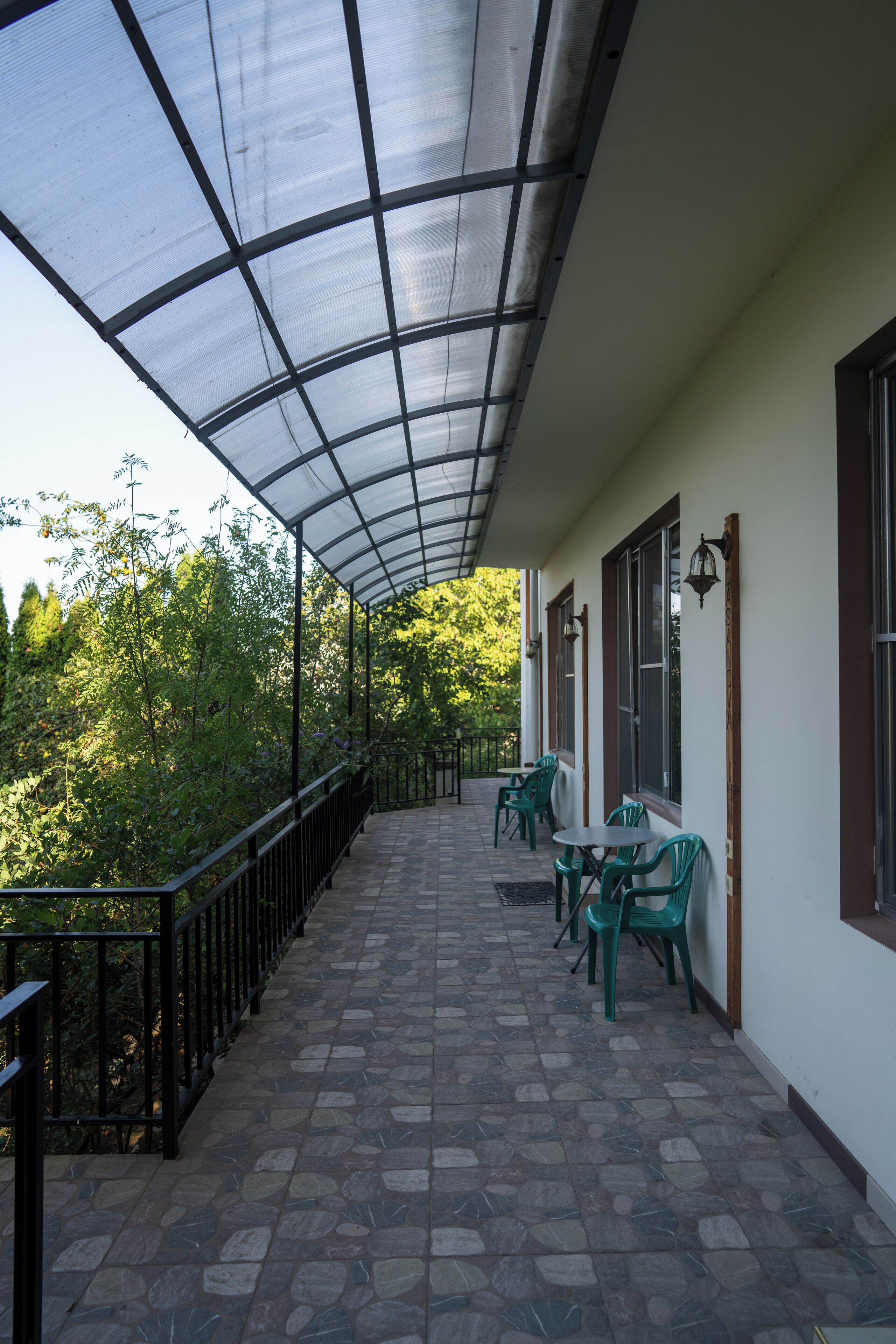 A covered outdoor area with a tiled floor, green chairs, and a table.