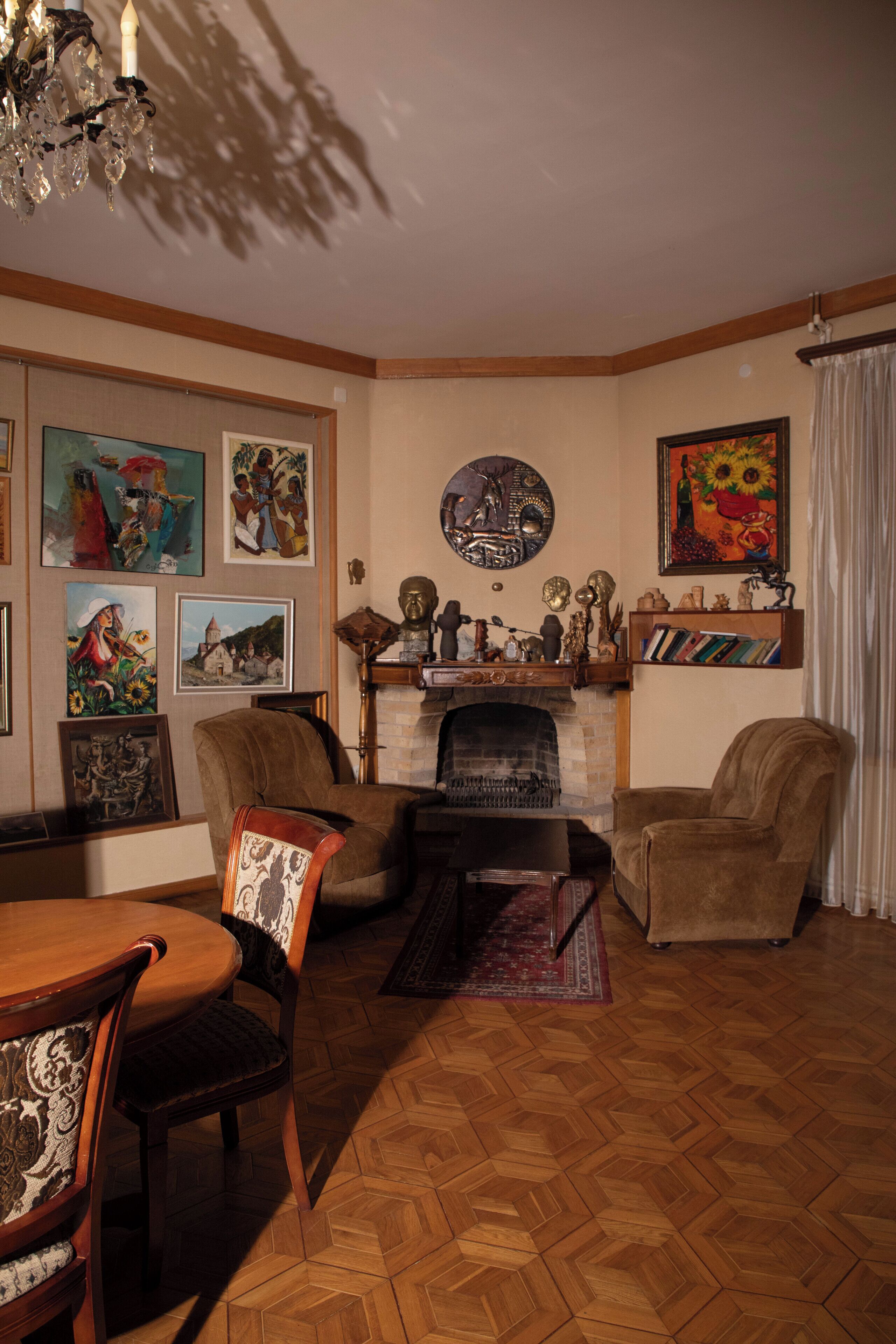 A living room with a fireplace, wooden flooring, and various framed artworks on the walls.