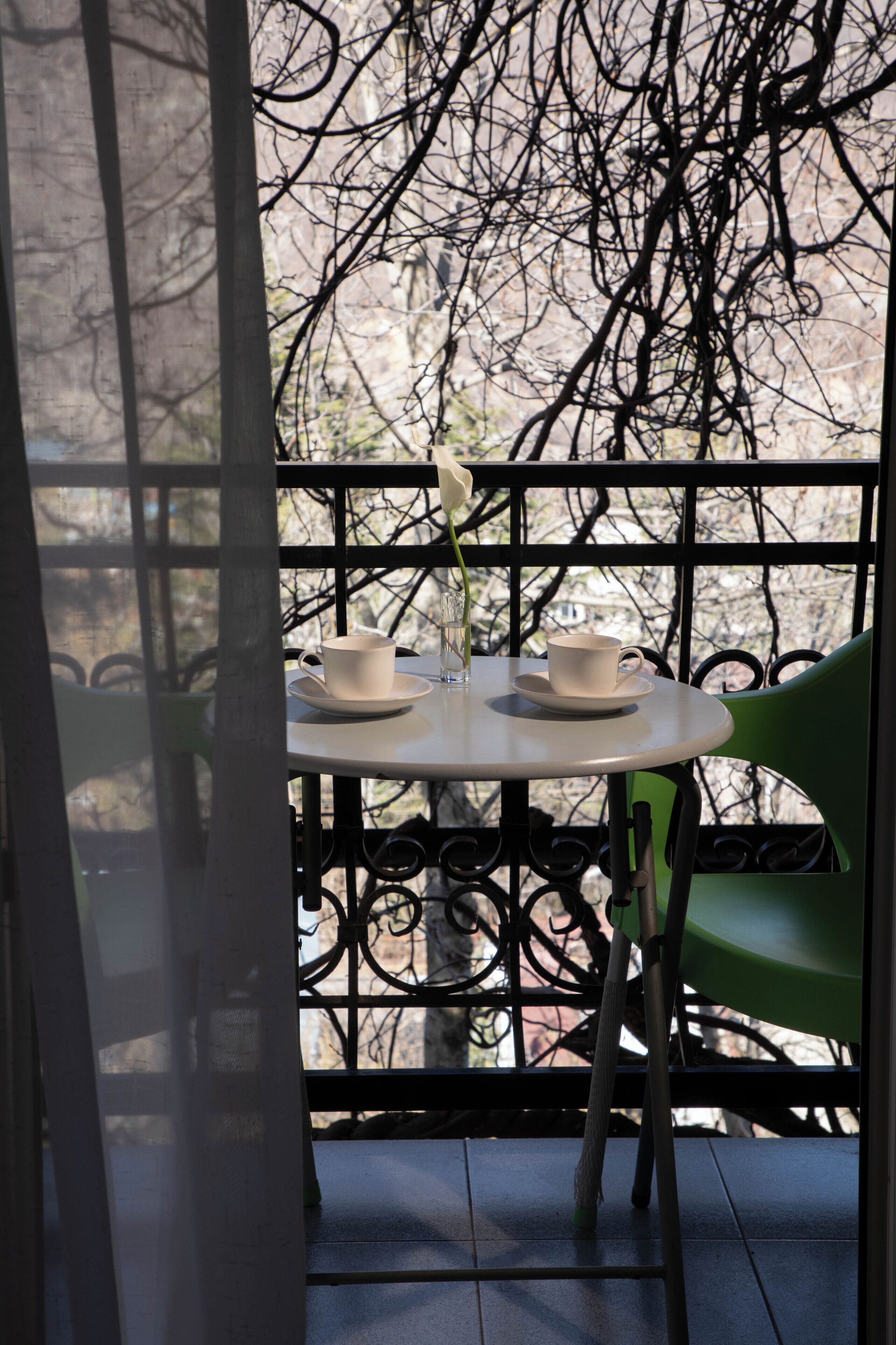 A balcony with a table and chairs, two cups, and a vase.