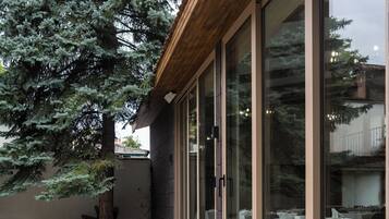 Un patio al aire libre con mesas y sillas redondas, ventanas amplias y un árbol.