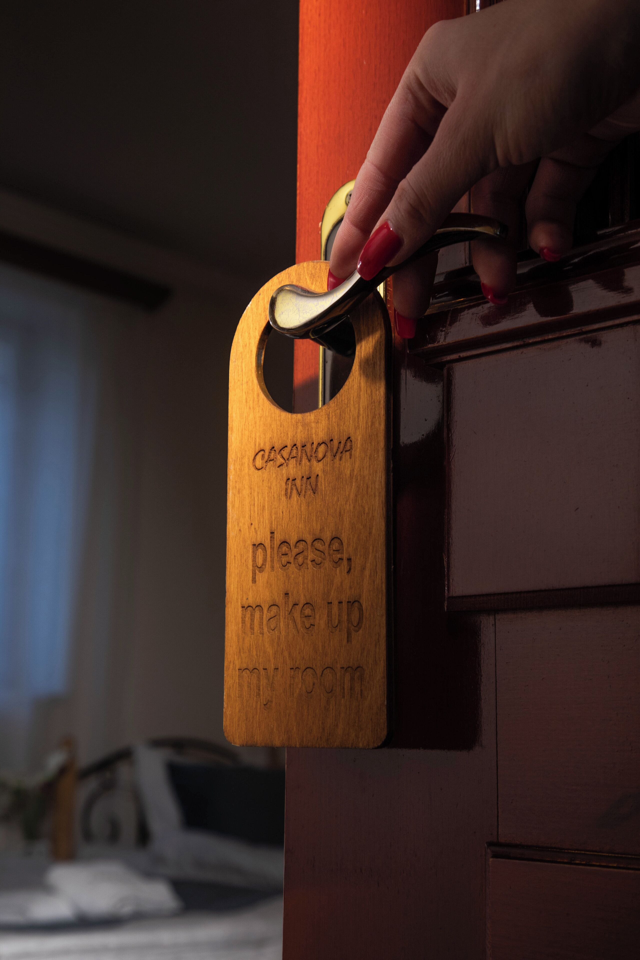 A hand holding a key, inserting it into a door with a wooden sign that reads "CASANOVA INN please, make up my room."