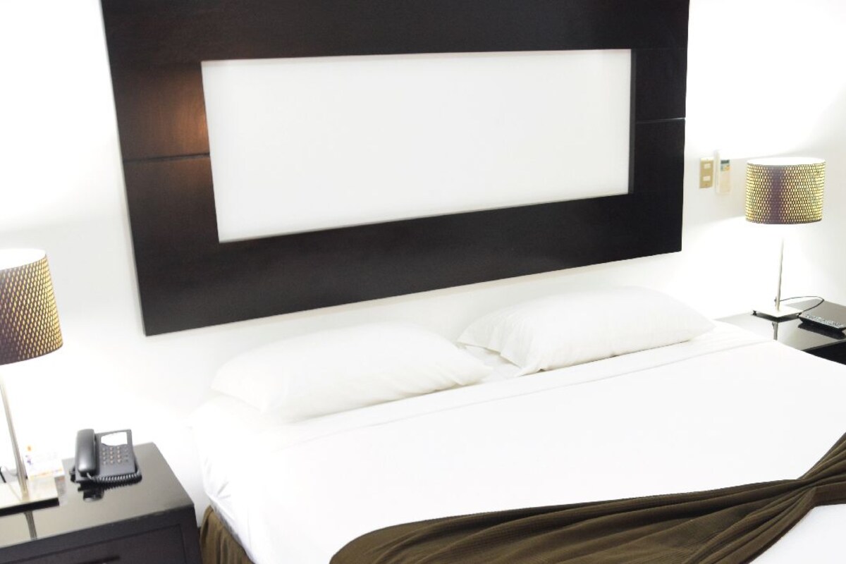 Ein Hotelzimmer mit einem großen Bett, zwei Nachttischen, einer Lampe und einem Telefon auf einem der Tische.