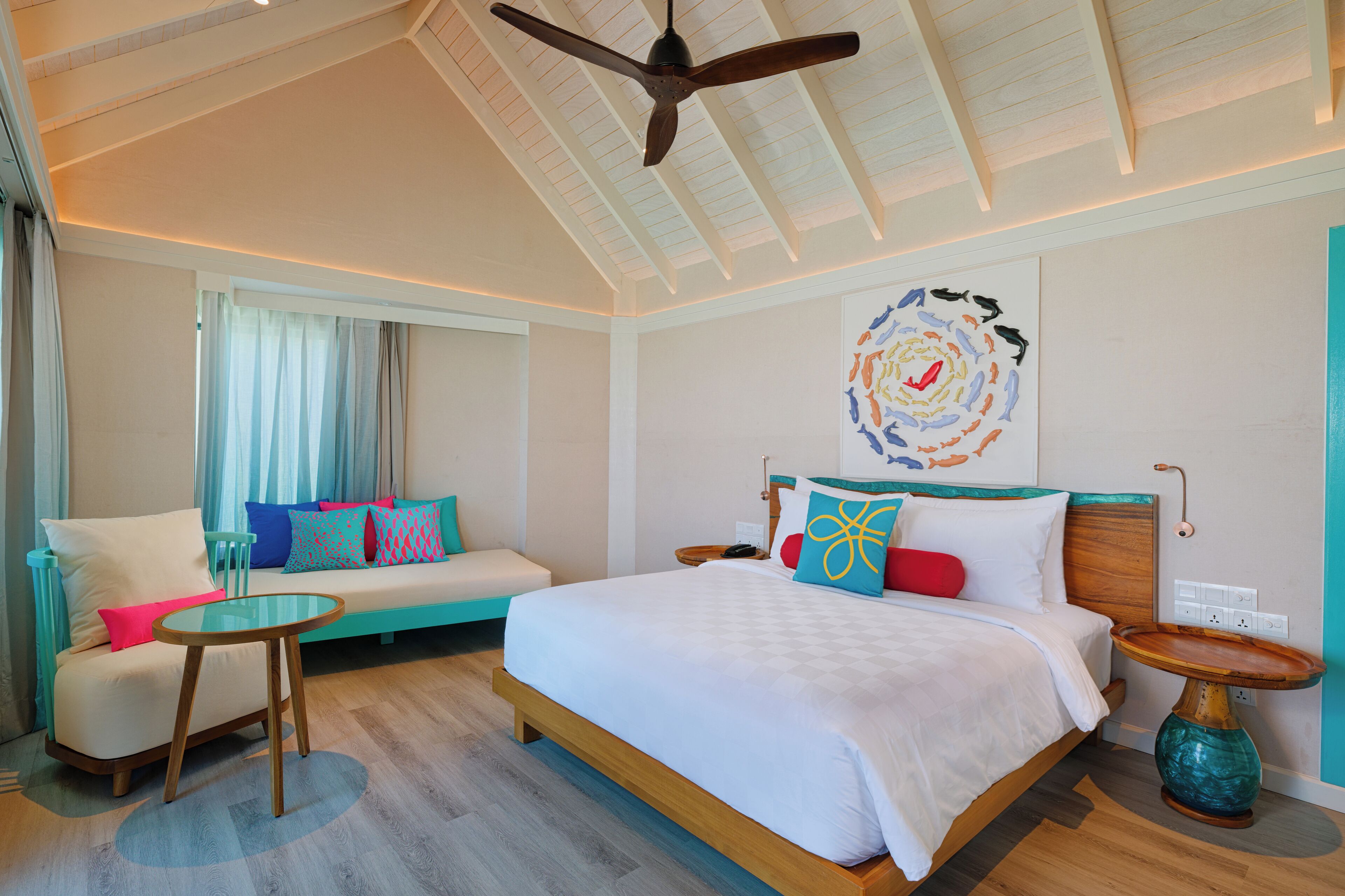 A modern hotel room with a large bed, a sofa, a small table, and a ceiling fan.
