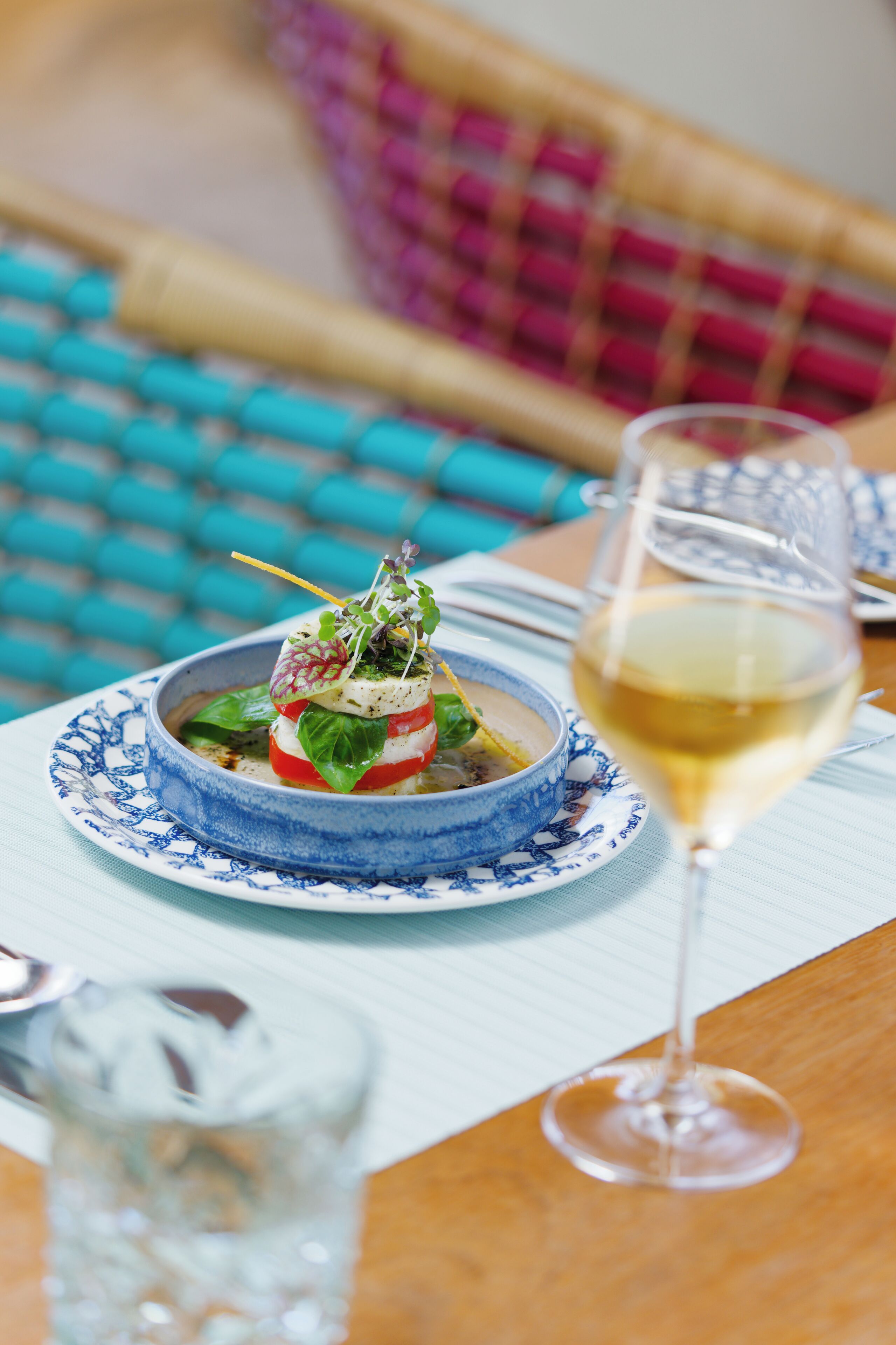 A dining table with a blue and white plate, a glass of white wine, and a glass of water.