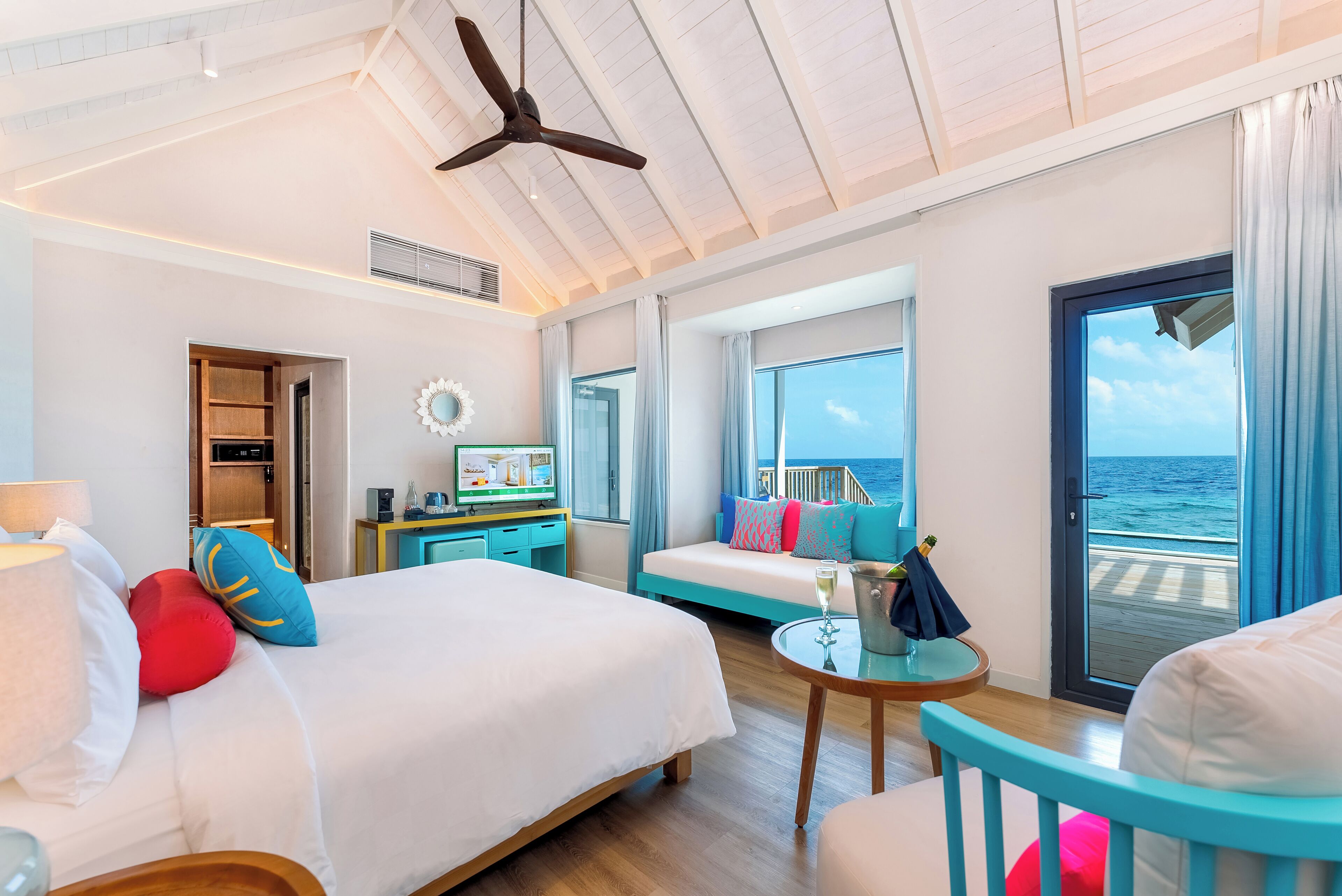 A spacious room with a large bed, a seating area with a view of the ocean, and a balcony with a door leading outside.