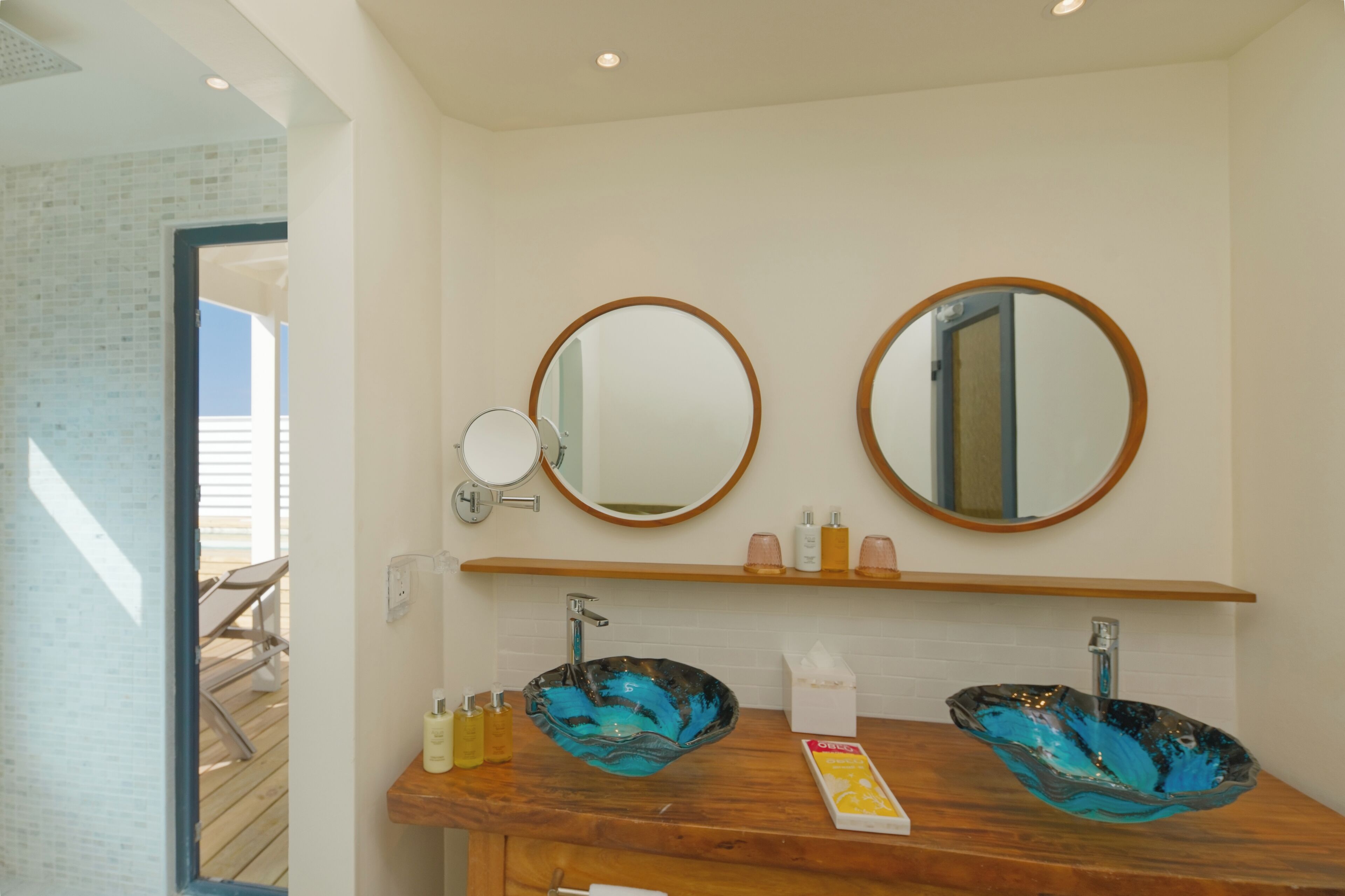 Ein Badezimmer mit zwei runden Spiegeln, einem Holzbadezimmermöbel und einem Waschbecken aus Glas.