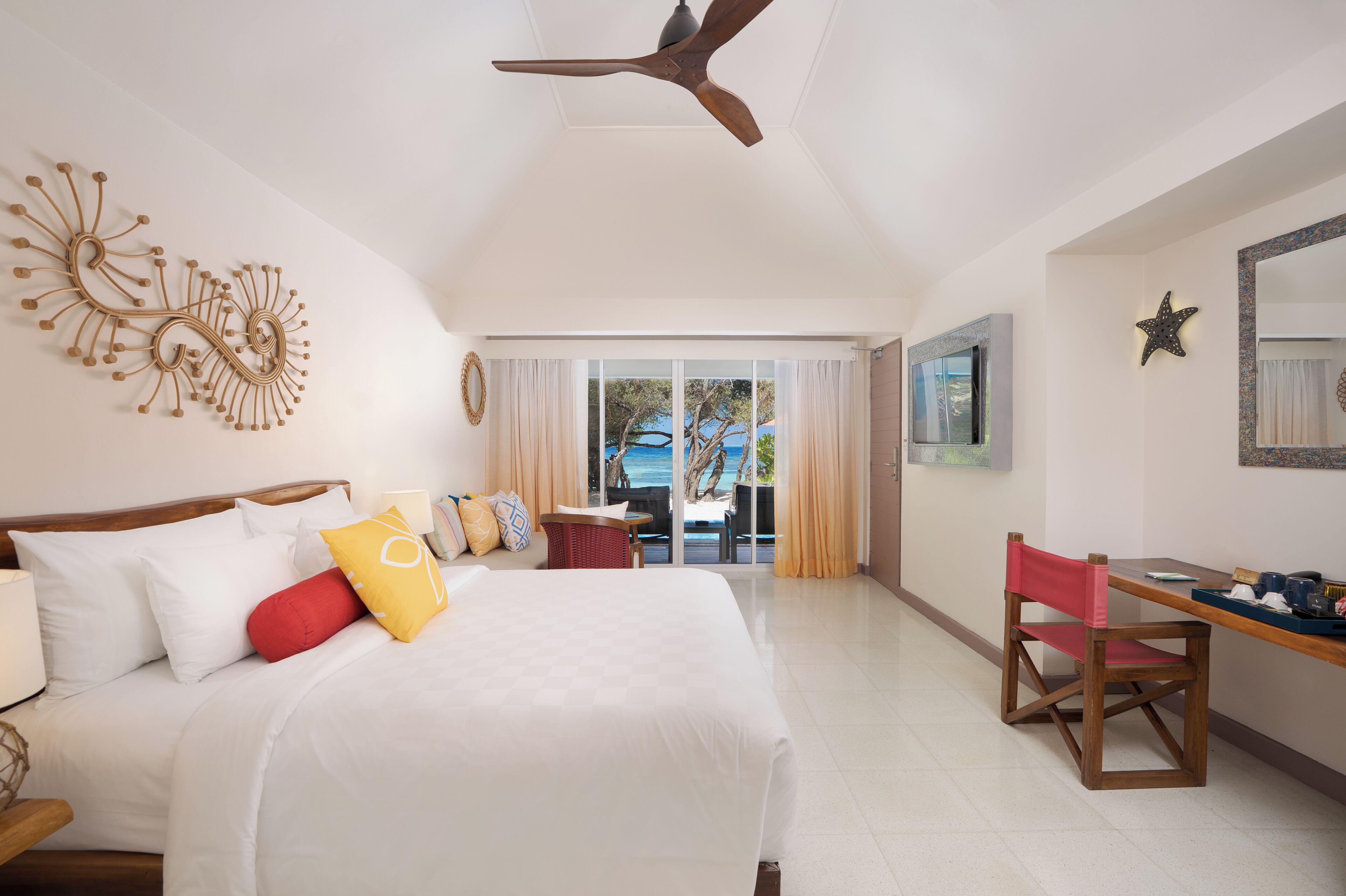 Habitación de hotel con cama, escritorio, silla, ventilador de techo y vistas al exterior.
