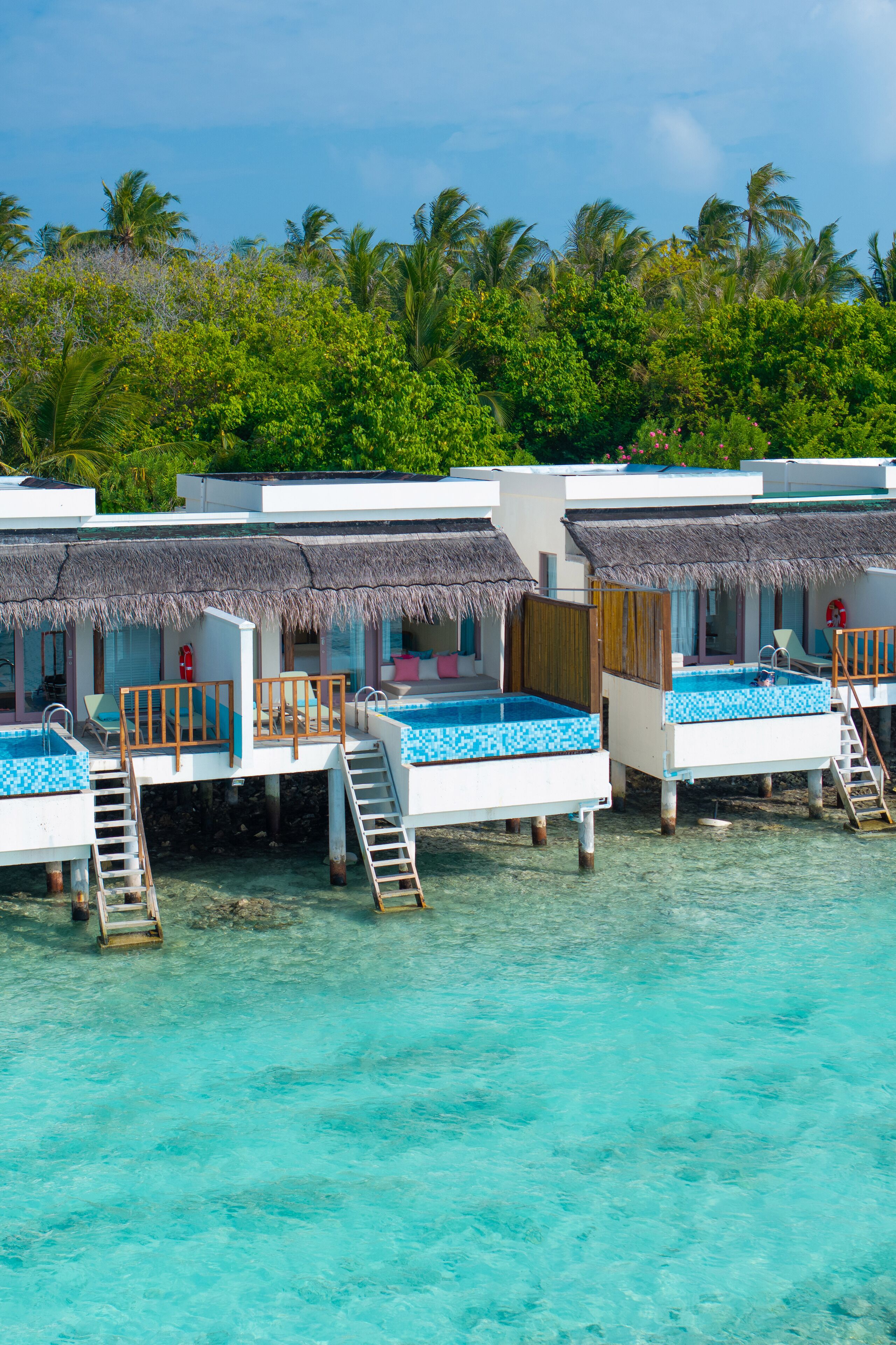 Overwater bungalows with thatched roofs, clear turquoise water, and lush greenery in the background.