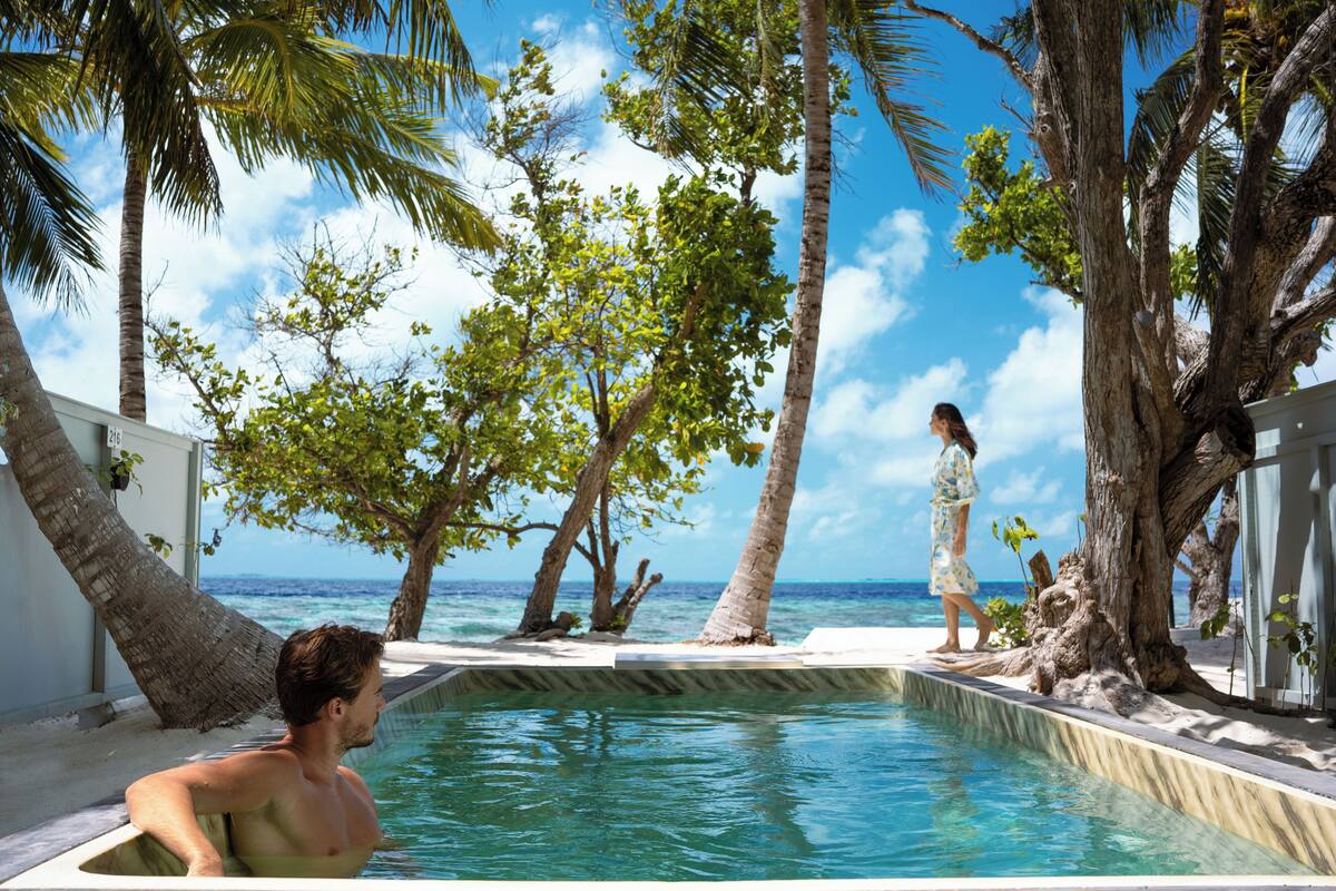 Un espace aménagé au bord de la piscine, offrant une vue sur l’océan, entouré de palmiers et surplombant un ciel dégagé.