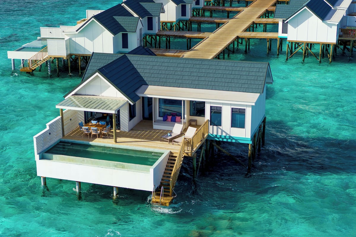 Un bungalow sur pilotis doté d’une piscine privée, d’une terrasse en bois et de plusieurs niveaux reliés par un pont.
