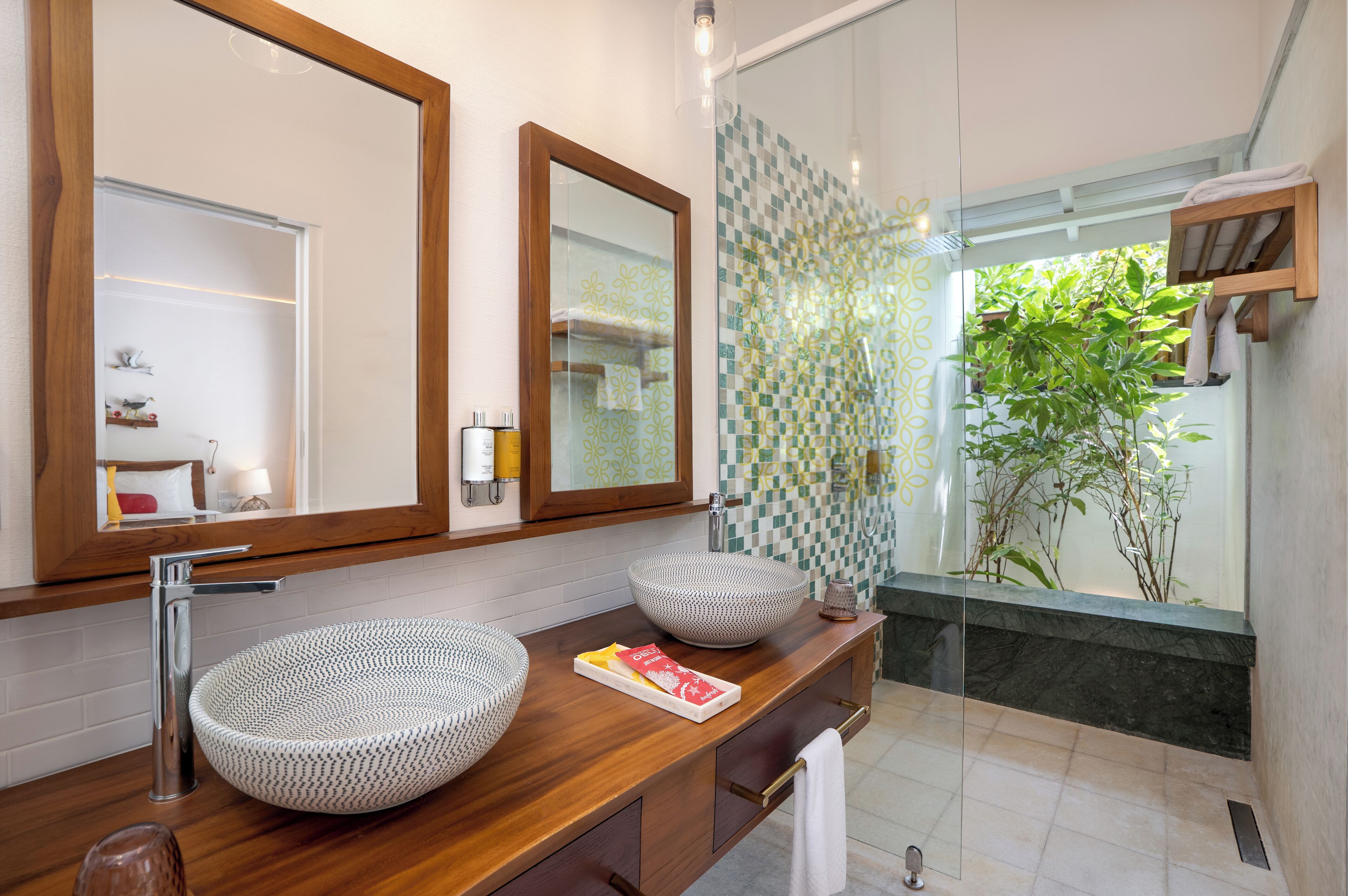 Een moderne badkamer met twee ronde wastafels, een houten wastafelmeubel, een grote spiegel en een douche met glazen deur.