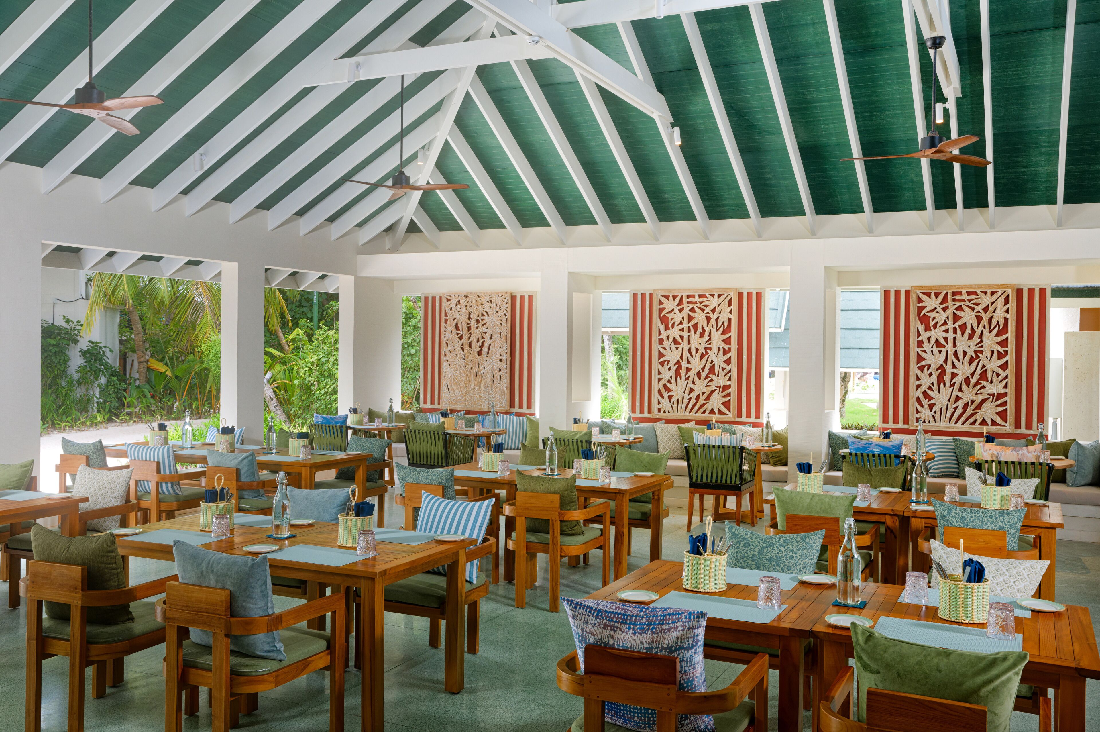 A spacious indoor dining area with wooden tables and chairs, large windows with green views, and decorative screens.