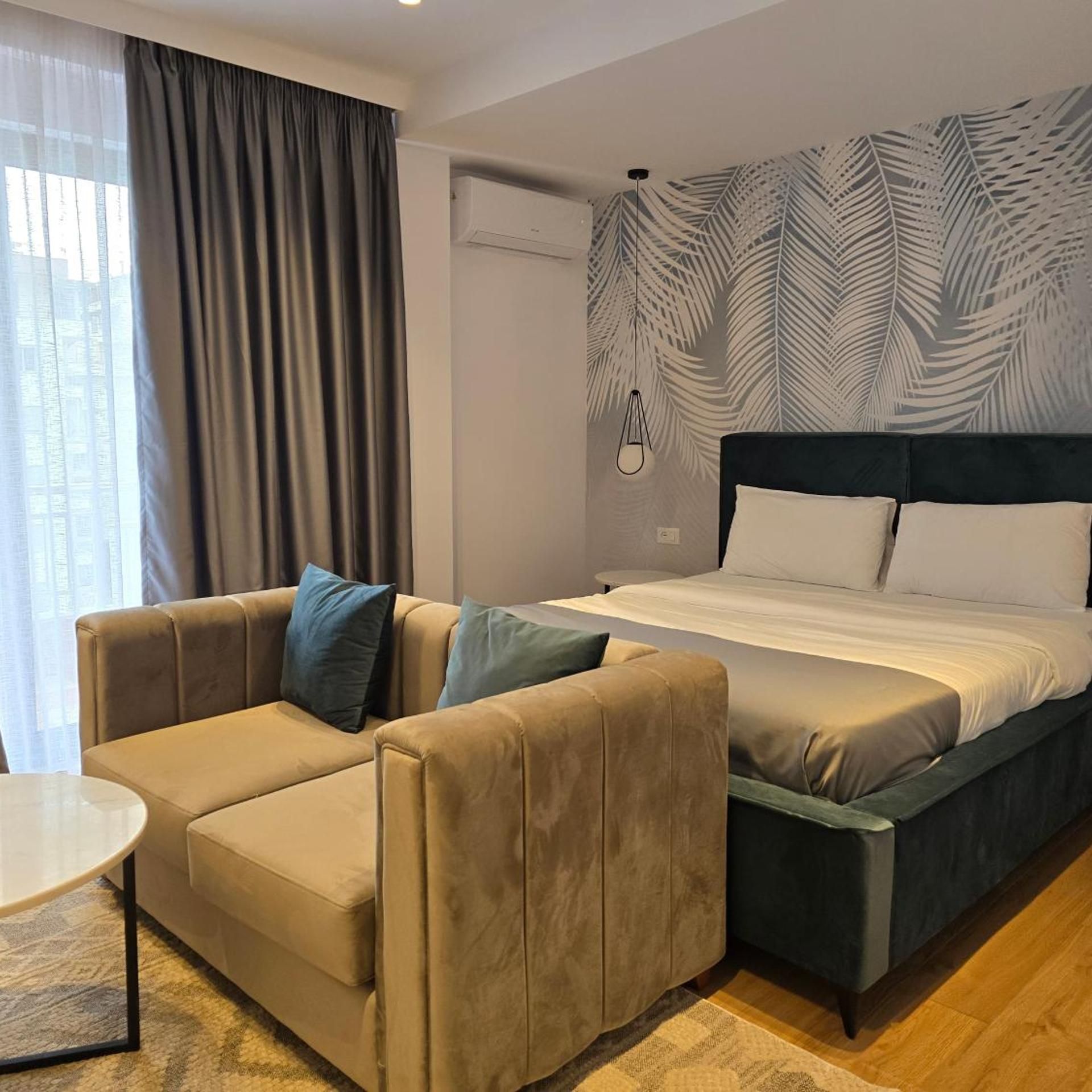 Habitació d'hotel amb un llit, un sofà, una taula petita i una finestra amb cortines.
