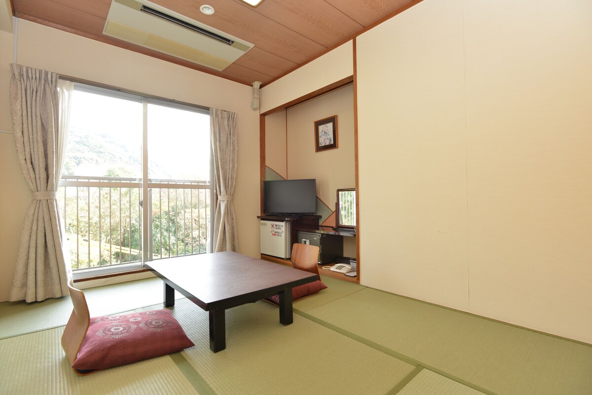 Een traditionele Japanse kamer met tatami vloerbedekking, een lage tafel, een televisie en een klein kastje.