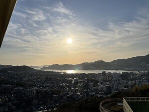 A cityscape with a bridge in the distance, buildings, and a body of water under a clear sky. - Yataro & Yataro Minamikan (Nagasaki)