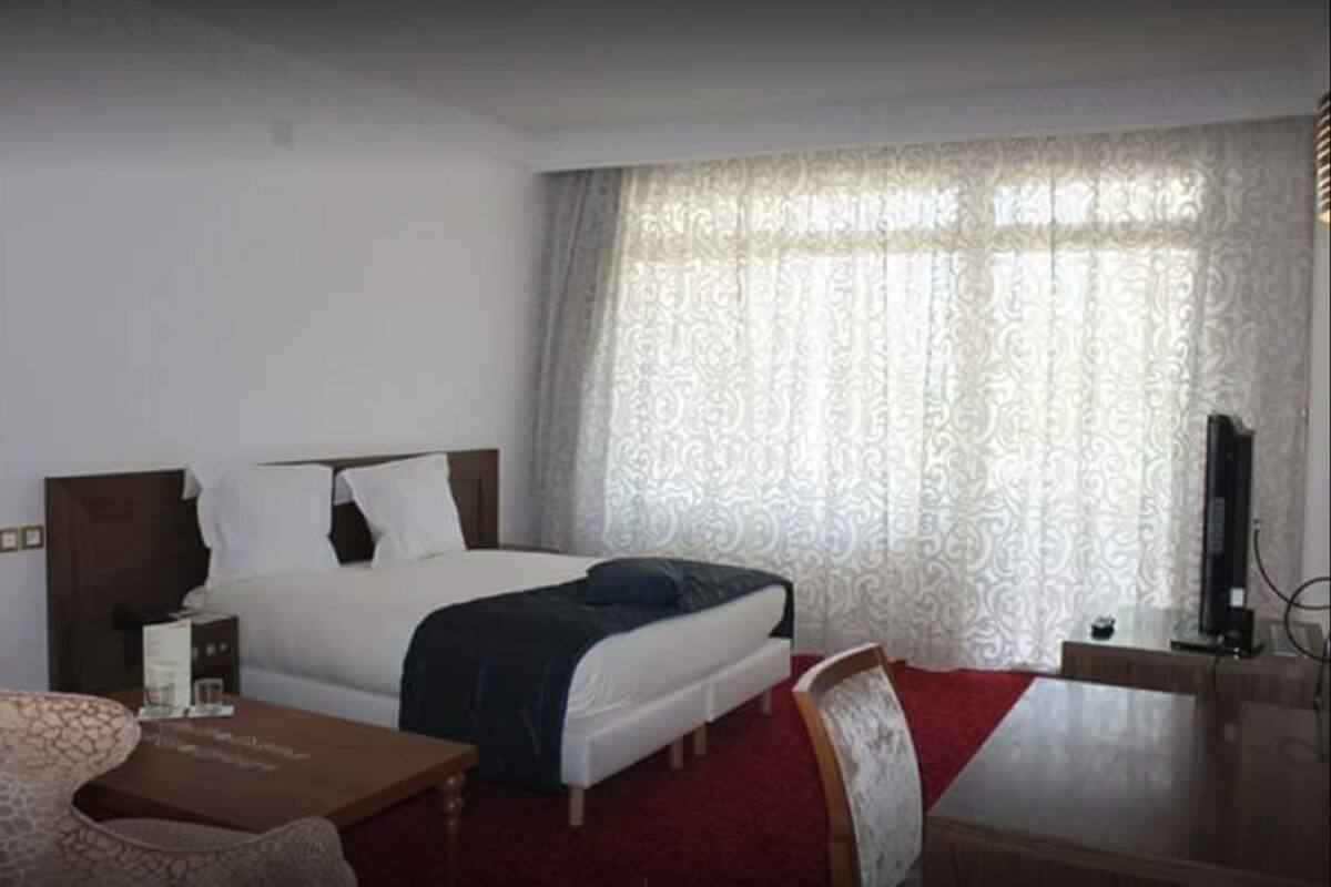 Hotellihuone, jossa on sänky, työpöytä, tuoli, televisio ja ikkuna, jossa on verhot.