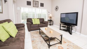 A living room with a brown sofa, green cushions, a wooden coffee table, a TV on a stand, and a patterned rug. - Glenbrook Homes (Clermont)