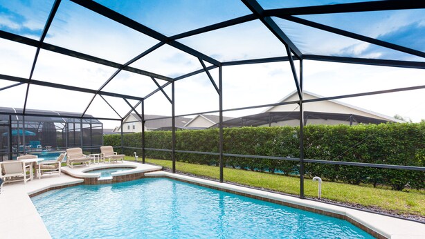 A swimming pool with a glass enclosure, lounge chairs, and a view of houses in the background. - Glenbrook Homes (Clermont)