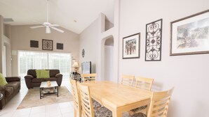 A spacious living room with a dining area, featuring a wooden table and chairs, a sofa, and a ceiling fan. - Glenbrook Homes (Clermont)
