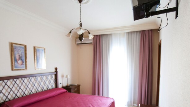 Une chambre d’hôtel avec un lit, un bureau, un téléviseur fixé au mur et une fenêtre avec des rideaux.