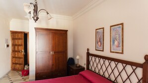 Une chambre à coucher avec une armoire en bois, un lit recouvert d’une courtepointe rouge et deux tableaux encadrés accrochés au mur.