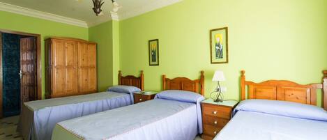 A room with two single beds, a wooden wardrobe, a nightstand with a lamp, and a door leading to a bathroom.