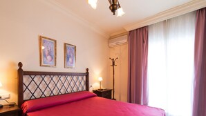 Une chambre d’hôtel avec un lit, deux tableaux accrochés au mur, un appareil de climatisation, une lampe sur pied et une fenêtre avec des rideaux.