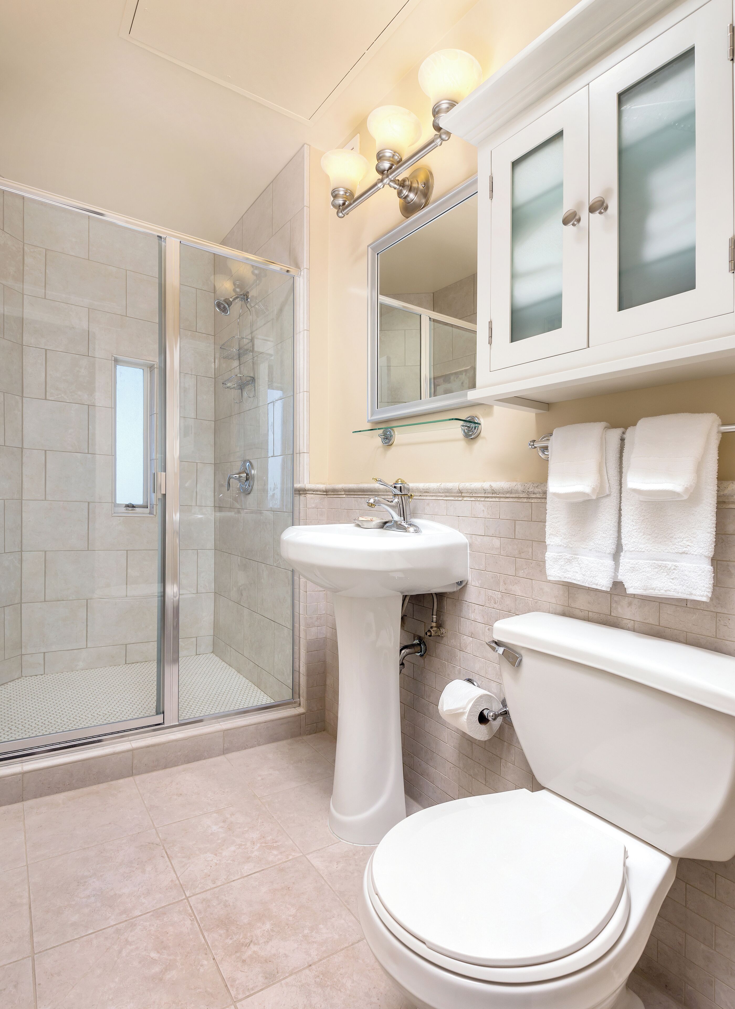 Une salle de bain avec une douche à parois de verre, un lavabo sur colonne, des toilettes et un meuble-lavabo avec un miroir et des placards.
