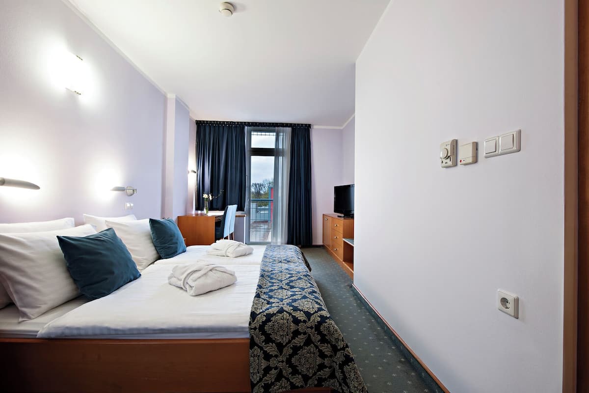 A hotel room with a bed, a desk, a television, and a balcony with curtains.