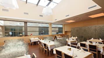 A restaurant with multiple tables and chairs, large windows, and a high ceiling with skylights.