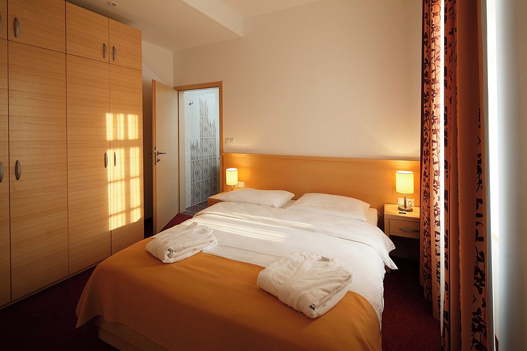 A hotel room with a bed, bedside tables, a wardrobe, and a door with a view.